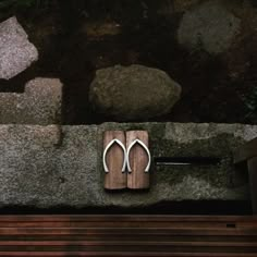 a pair of white scissors sitting on top of a wooden board next to a stone wall