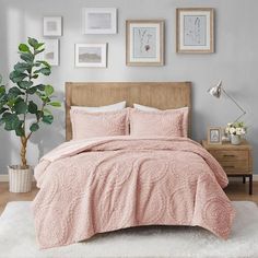 a bed with pink comforter and pillows in a bedroom next to a potted plant