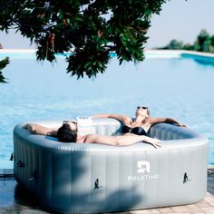 two people laying in an inflatable pool next to the water