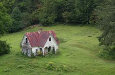 an old abandoned house in the middle of a green field surrounded by trees and bushes