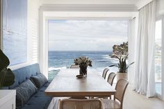 a dining room table with chairs and a vase on it in front of a window overlooking the ocean