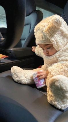 a baby sitting in the back seat of a car wearing a teddy bear costume and drinking from a bottle