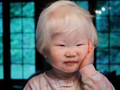 a young child with blonde hair is holding his hand up to his face and looking at the camera