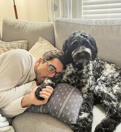 a man laying on top of a couch next to a black dog holding a pillow