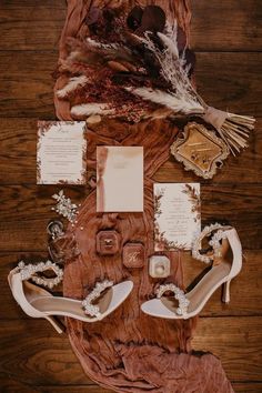 wedding stationery and shoes laid out on a wooden floor with lace, feathers, pearls, and paper