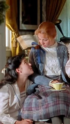 two women are sitting on a couch and one woman is holding a cup in her lap