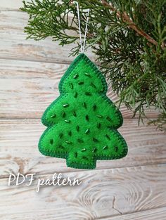 a felt christmas tree ornament hanging from a pine tree branch on a wooden background