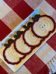 three crocheted apples on a white plate sitting on a red checkered tablecloth