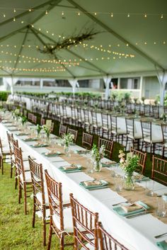 tables set up for an event under a tent with string lights and greenery on the ceiling