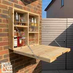 a wooden shelf with bottles and glasses hanging from it's back wall next to a brick building