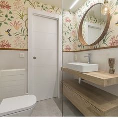 a bathroom with floral wallpaper and wooden countertop, white toilet and sink under a round mirror