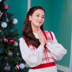 a young woman standing in front of a christmas tree with her hands clasped to her chest