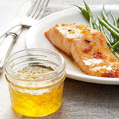 a white plate topped with salmon and green beans next to a jar of honey syrup