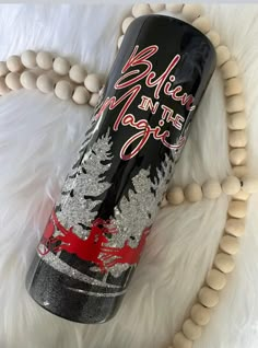 a black bottle with silver glitters on it sitting next to a beaded necklace