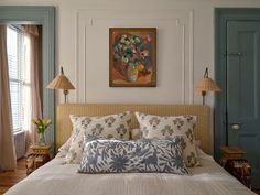 a bed with two lamps on either side of it and a painting above the headboard