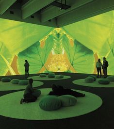 two people are sitting on bean bags in front of a large screen with green leaves