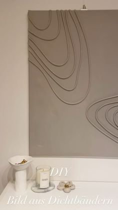 a white table topped with two candles next to a wall mounted art piece on the wall