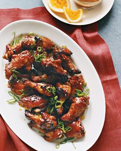 a white plate topped with chicken wings covered in sauce and garnished with green onions