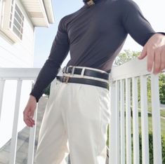 a man standing on a porch with his hands in his pockets and wearing white pants