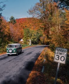 an old vw bus driving down the road in front of a speed limit sign