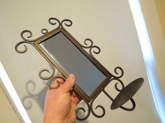 a hand holding a mirror in front of a wall mounted hook on a white wall