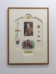 a white framed photo with many different items on the bottom and sides, in front of a white wall