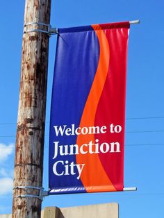 a welcome to junction city sign hanging on a telephone pole with a blue sky in the background