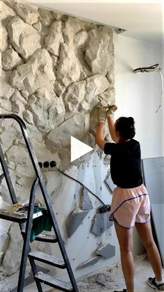 a woman in black shirt and pink shorts painting a stone wall with paint rollers