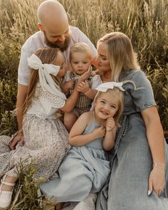 a man and two women are sitting with their children on the grass in front of some tall grass