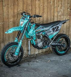 a dirt bike parked in front of a wooden fence with graffiti on it's side