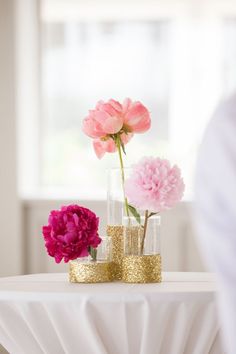 pink flowers are in vases on a table with gold glitter accents and white drapes