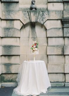 a wedding cake sitting on top of a table next to a stone wall with a statue