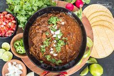 a bowl of chili with tortillas, limes and cilantro on the side