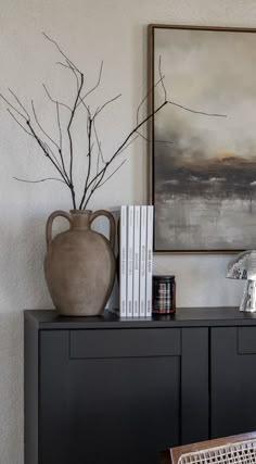 a vase sitting on top of a black cabinet next to a table with two books