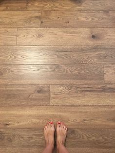 a person standing on a wooden floor with their feet up in the air and red nail polish