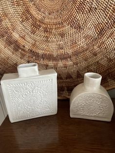 two white vases sitting on top of a wooden table next to a woven basket