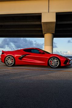 a red sports car is parked under an overpass in front of the ocean and sky