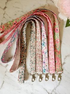 six floral lanyards on a marble counter with pink flowers in the back ground