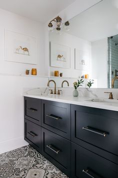 a bathroom with double sinks and black cabinetry, gold handles on the faucets