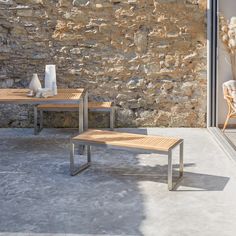 two wooden benches sitting next to each other near a stone wall and window sill