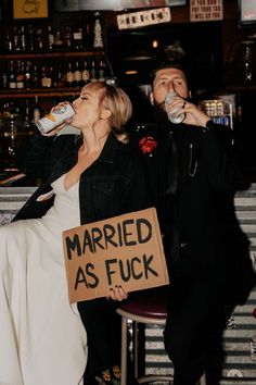 a man and woman sitting at a bar drinking from bottled beverages, one holding a sign that says married as fock