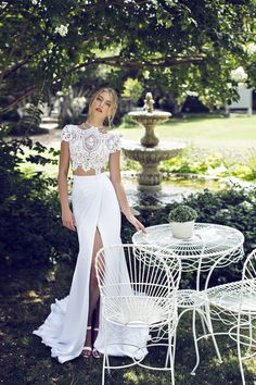 a woman standing next to a white table and chair in front of a garden area