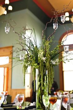 a tall vase filled with flowers and greenery sitting on top of a wooden table