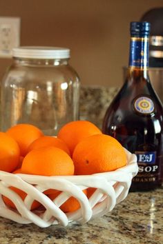 a white bowl filled with oranges on top of a kitchen counter next to bottles