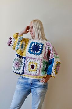 a woman standing in front of a wall wearing a crocheted granny's sweater