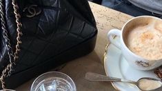 there is a cup of coffee next to a purse and two glasses on the table