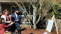 a group of people standing in front of a house with an easel on the ground