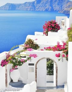 a white building with pink flowers on the roof and blue water in the back ground