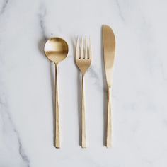 three forks, two spoons and one knife on a white marble countertop with gold colored utensils