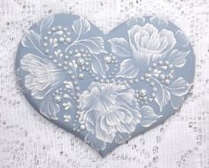 a blue heart with white flowers and pearls on the inside is sitting on a lace tablecloth